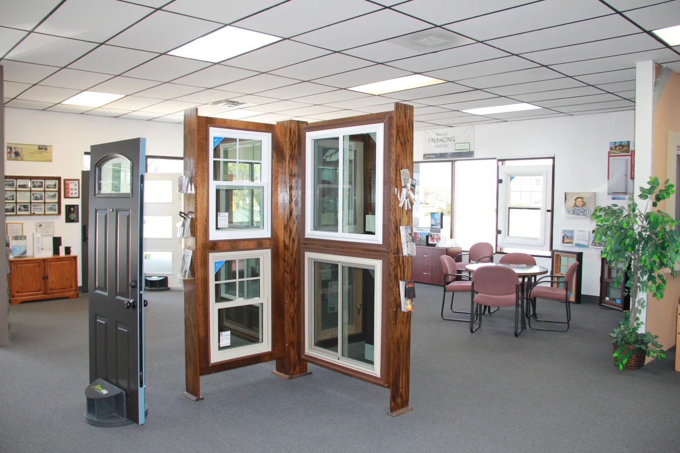 A wide open section of the Peakview Windows, Siding & Stucco showroom in Colorado Springs showing different full-size doors, installed full-size windows installed in a large wood display, a table with four comfortable chairs, and lots of other things on the walls.