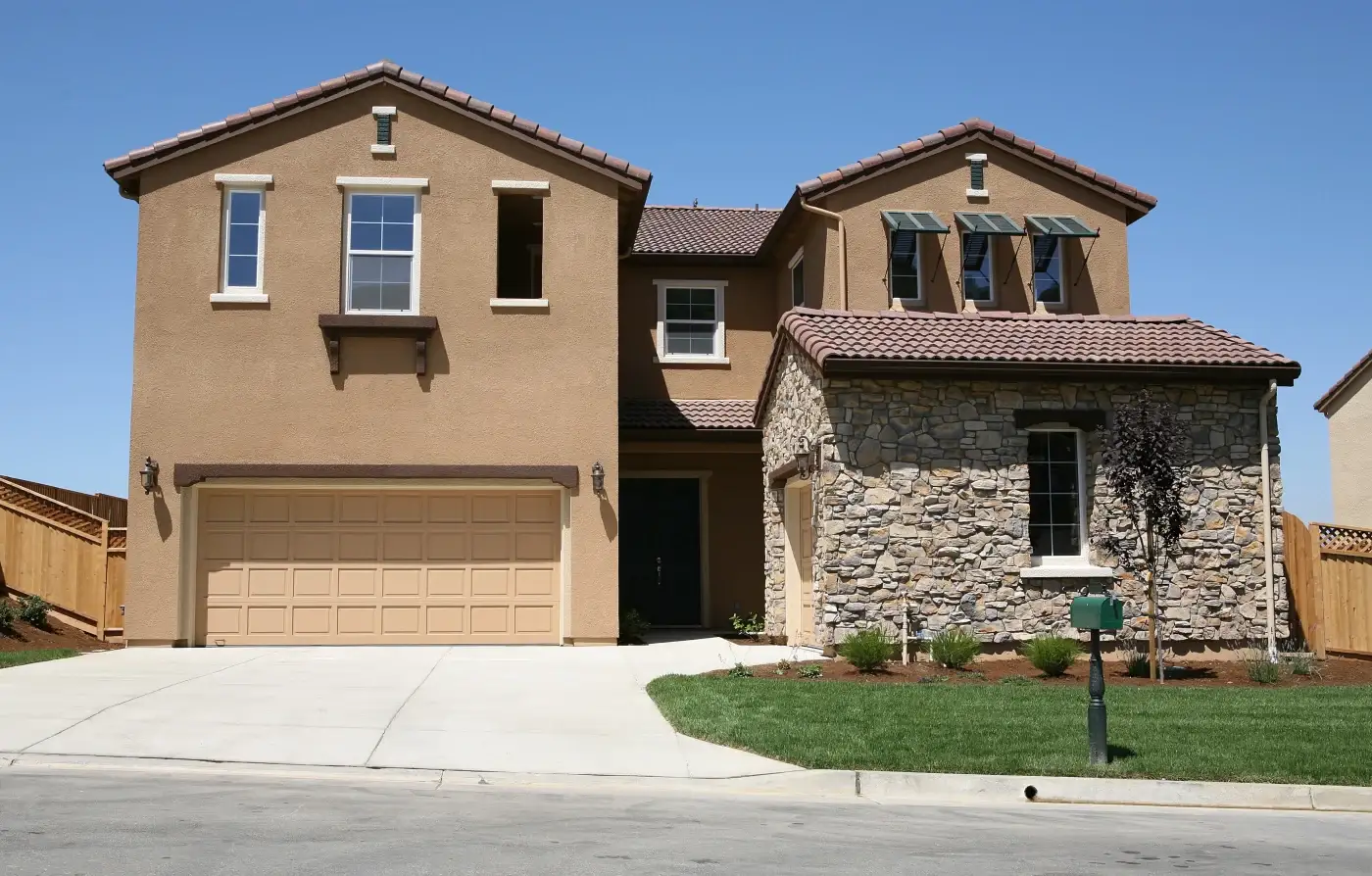 A lovely two-story residence mainly covered with a light brown stucco, with a small covered garage in the front with stone veneer siding.