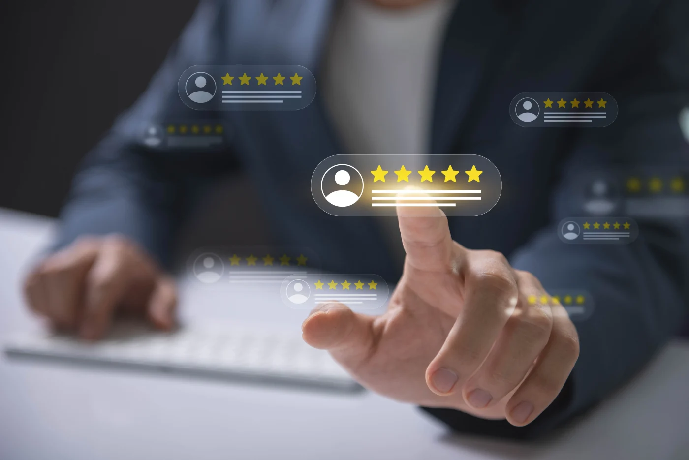 There are icons representing user profiles floating through the air in front of a man sitting at his computer desk with a few lines signifying text and five stars for a great review. He’s reaching out with his left hand and touching one with his pointer finger.