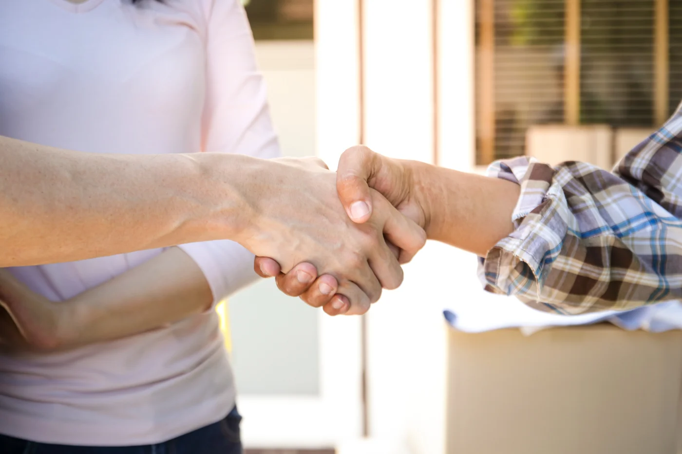 A friendly exterior remodeling contractor shaking hands with a man and introducing himself to the man and his wife outside the entryway to their home.