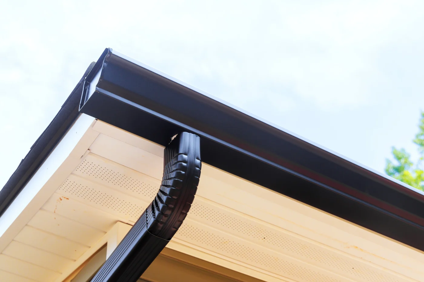 Residential Gutter Repair & Gutter Installation Services In Colorado Springs Close-up of new black gutters and a downspout with white soffit and fascia showing.