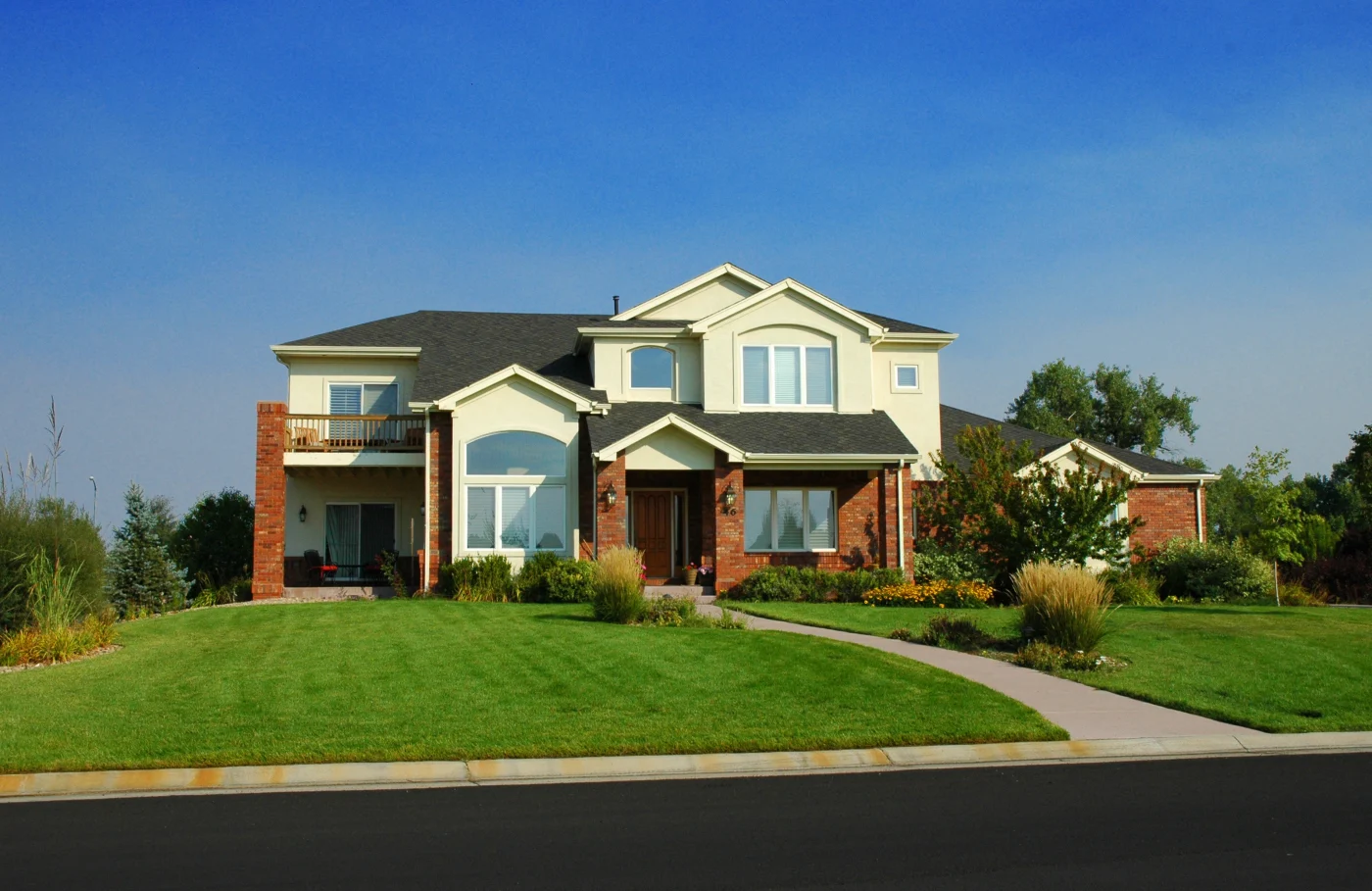 A beautiful two-story home in Colorado with a modern exterior design incorporating multi-level roofing, a variety of windows, a single-entry door, stone veneers around pillars and the base level of the home, as well as light yellow or beige stucco.