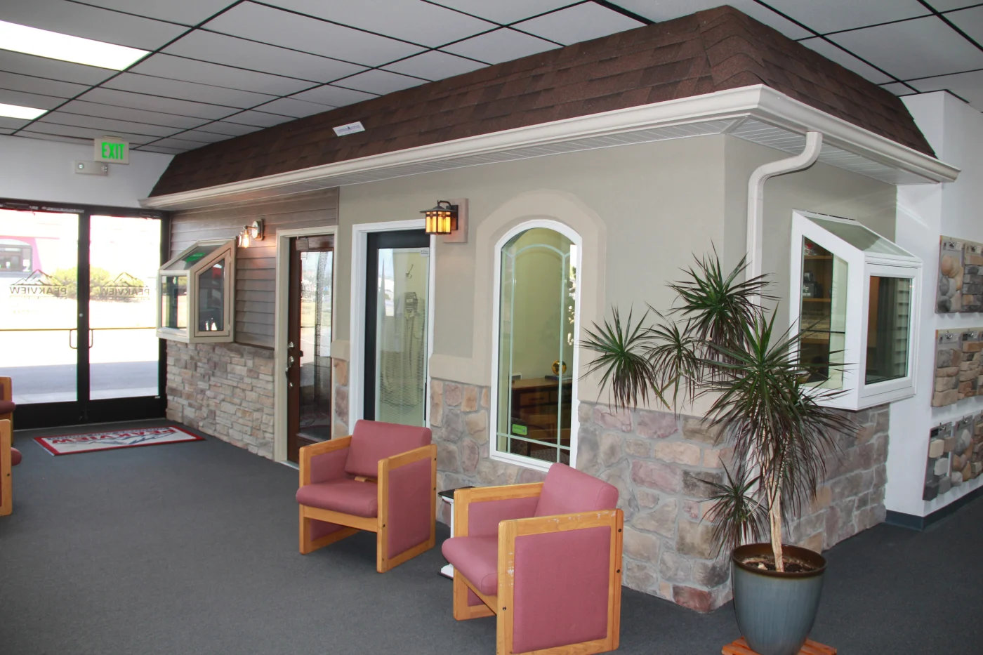 A large section of the Peakview Windows, Siding & Stucco showroom in Colorado Springs showing some waiting chairs in front of a wall with a stone veneer base, a stucco section, a section with fiber cement siding, different kinds of windows, an entry door, as well as soffit and gutters.