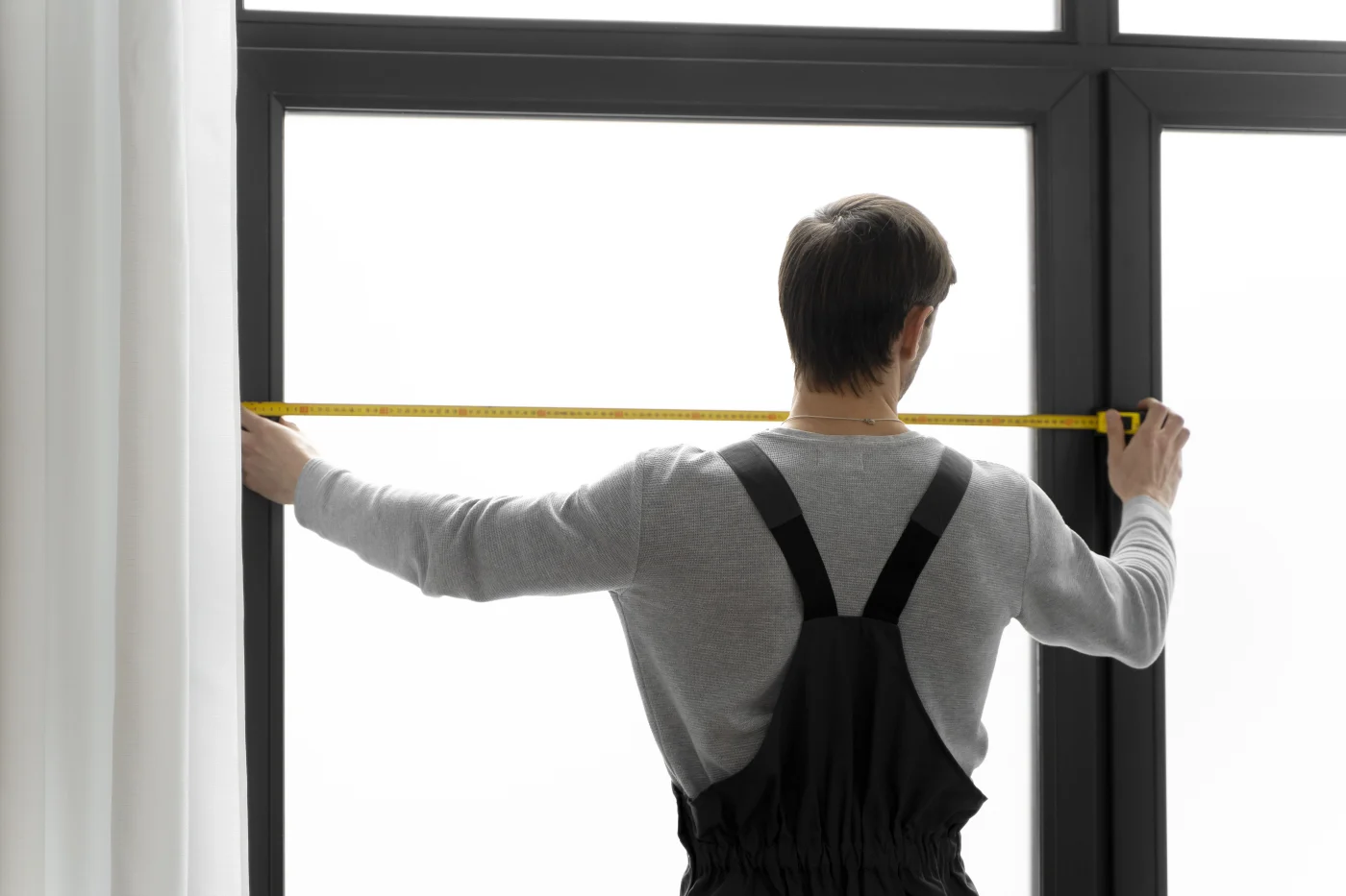 A certified window installer takes a precise window measurement.