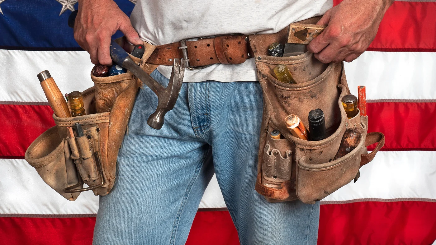 Close-up of a contractor wearing a fully stocked toolbelt in front of the American flag