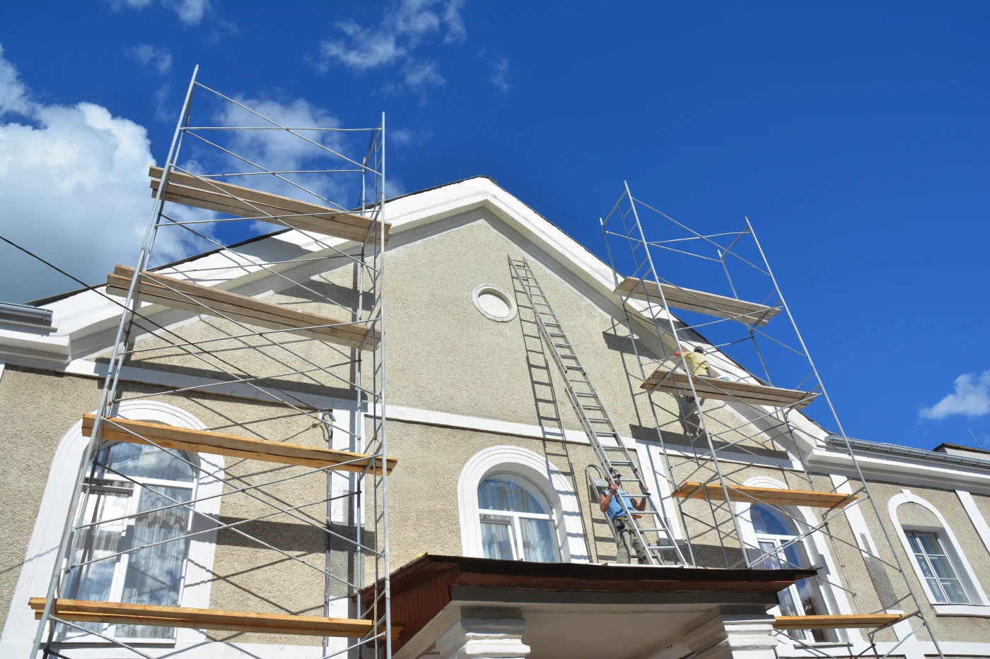 Ladders and scaffolds are set up next to a home while stucco is applied.