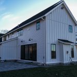 A large farmhouse with a flagstone patio, a porch, and white James Hardie siding.