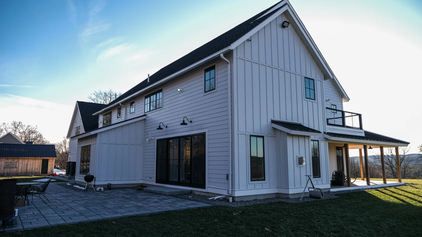 A large farmhouse with a flagstone patio, a porch, and white James Hardie siding.