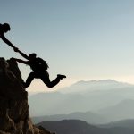 One climber helps another up a steep rock face