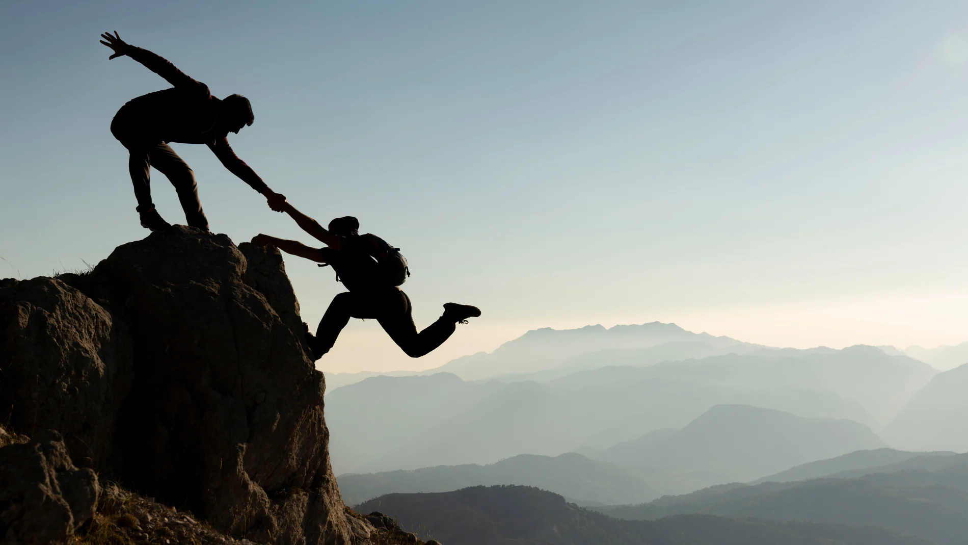 One climber helps another up a steep rock face