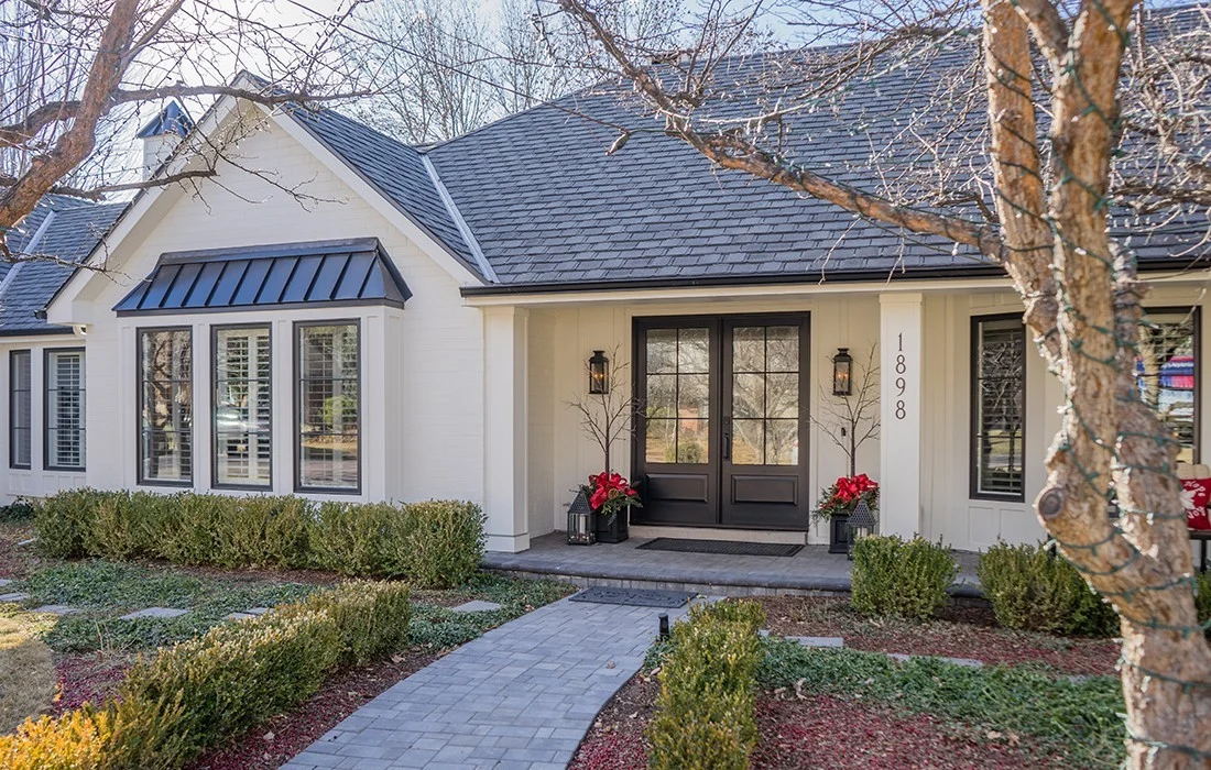 Single-story beige stucco home with tile roof, stone accents, and a front window with white shutters and a red flower box.