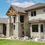 Two-story home in Fountain, CO with tan stucco and stone siding, a covered entry with columns, and a neatly landscaped front yard