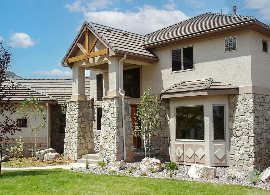 Two-story home in Fountain, CO with tan stucco and stone siding, a covered entry with columns, and a neatly landscaped front yard