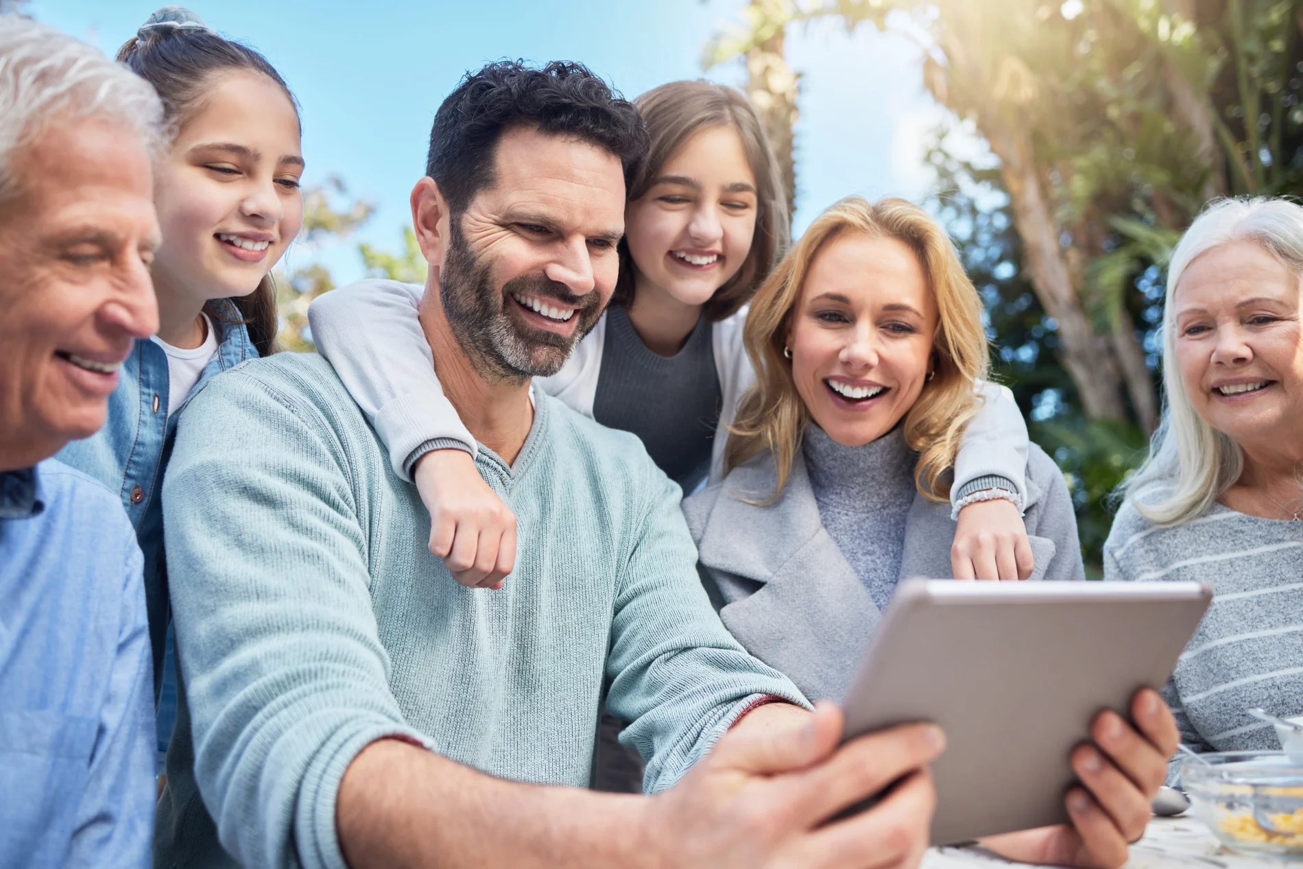 A multi-generational family crowds together to look into a tablet screen