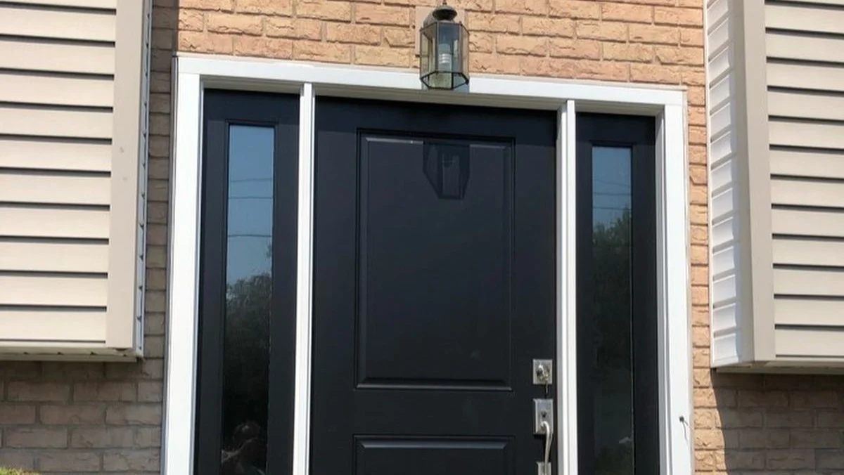 Black front entry door with tall glass sidelights on both sides, framed in white trim against a brick and siding exterior.