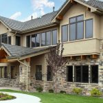 A sprawling modern home showcasing a stunning siding replacement that masterfully pairs smooth, earth-toned stucco panels with textured stone veneer accents along the lower level and entryway columns.