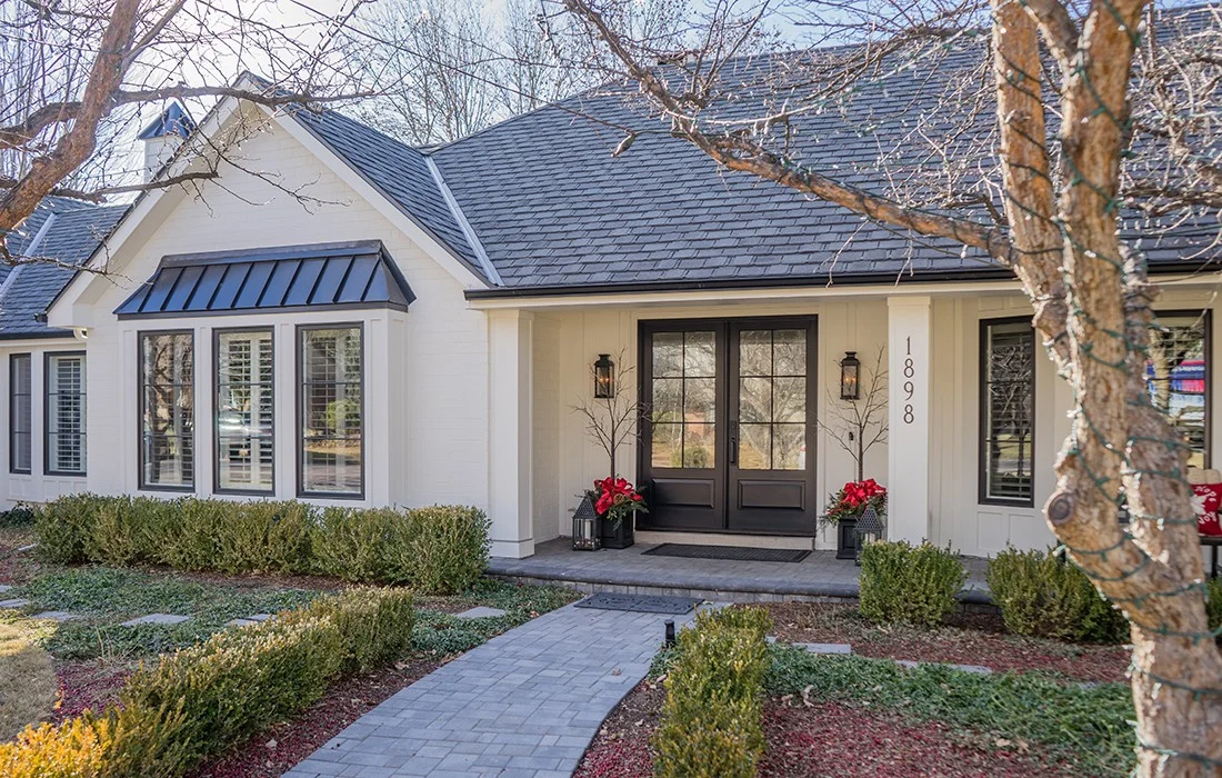 A stunning door installation featuring elegant black multi-pane double doors that create a welcoming focal point for this white farmhouse-style home and its paved walkway.