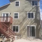 The side of a three-story tan house with white windows, white sliding glass doors, and stairs leading upstairs.
