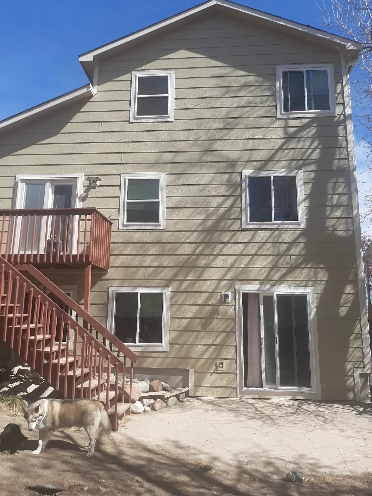 The side of a three-story tan house with white windows, white sliding glass doors, and stairs leading upstairs.