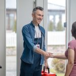 A homeowner shaking hands with a smiling contractor as he enters her home.