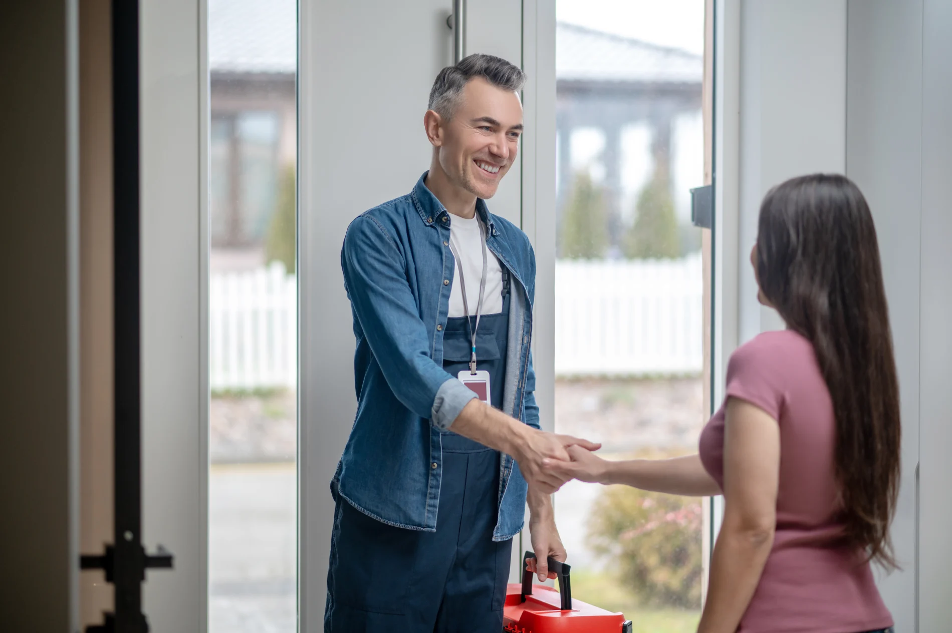 A homeowner shaking hands with a smiling contractor as he enters her home.