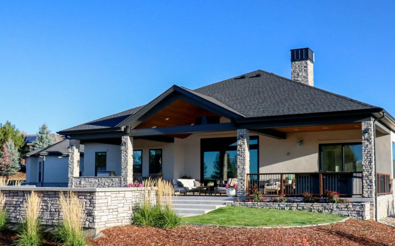 An expansive covered backyard patio, featuring wood-paneled ceilings and rugged stone pillars, beautifully highlights the smooth, neutral-toned exterior walls finished by professional stucco contractors.
