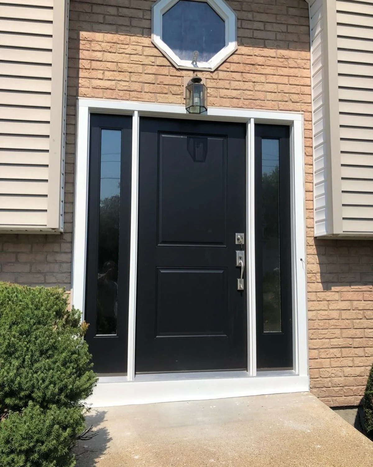 A modern black front door with matching side lites and clean white trim beautifully updates a residential brick entryway, highlighting professional door installation services.