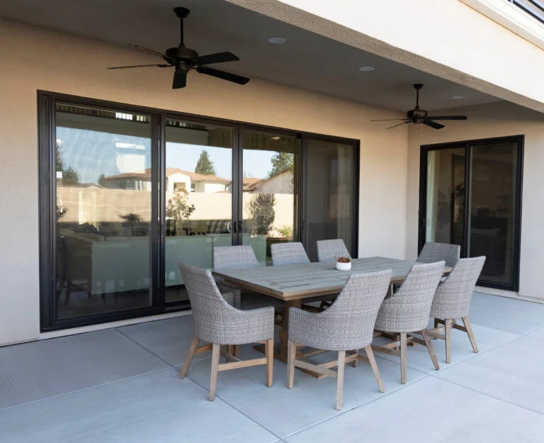 A covered concrete patio features an outdoor dining set positioned in front of large, dark-framed sliding glass doors completed by professional door installation services.