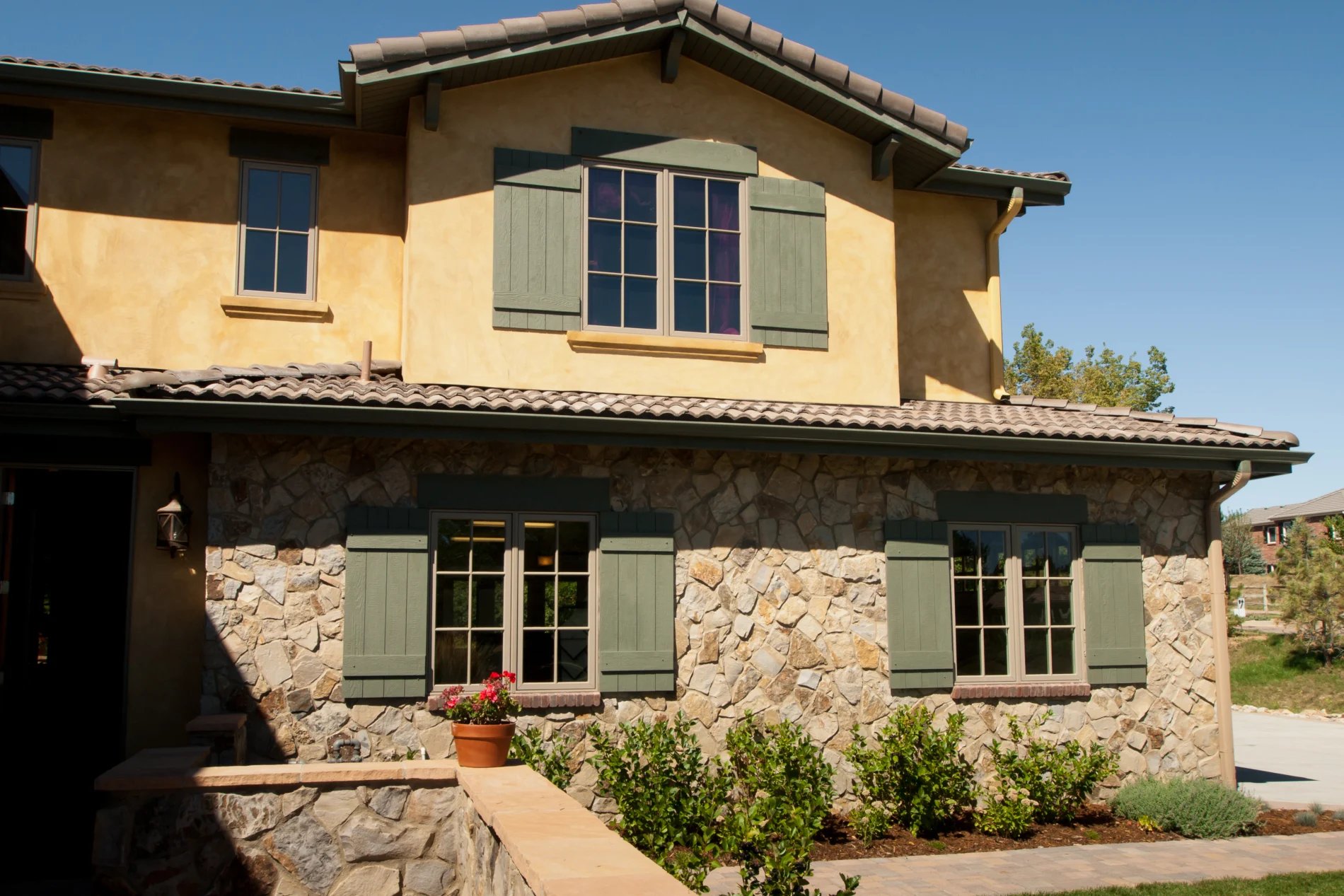 Luxury Living A close-up view of a two-story house with stone on the bottom floor and orange stucco on the upper floor, brown windows with brown shutters, and a tile roof.