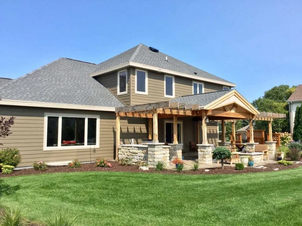 Earth-toned horizontal cladding beautifully complements the wooden pergola and stone patio of this spacious suburban home following a complete siding replacement.