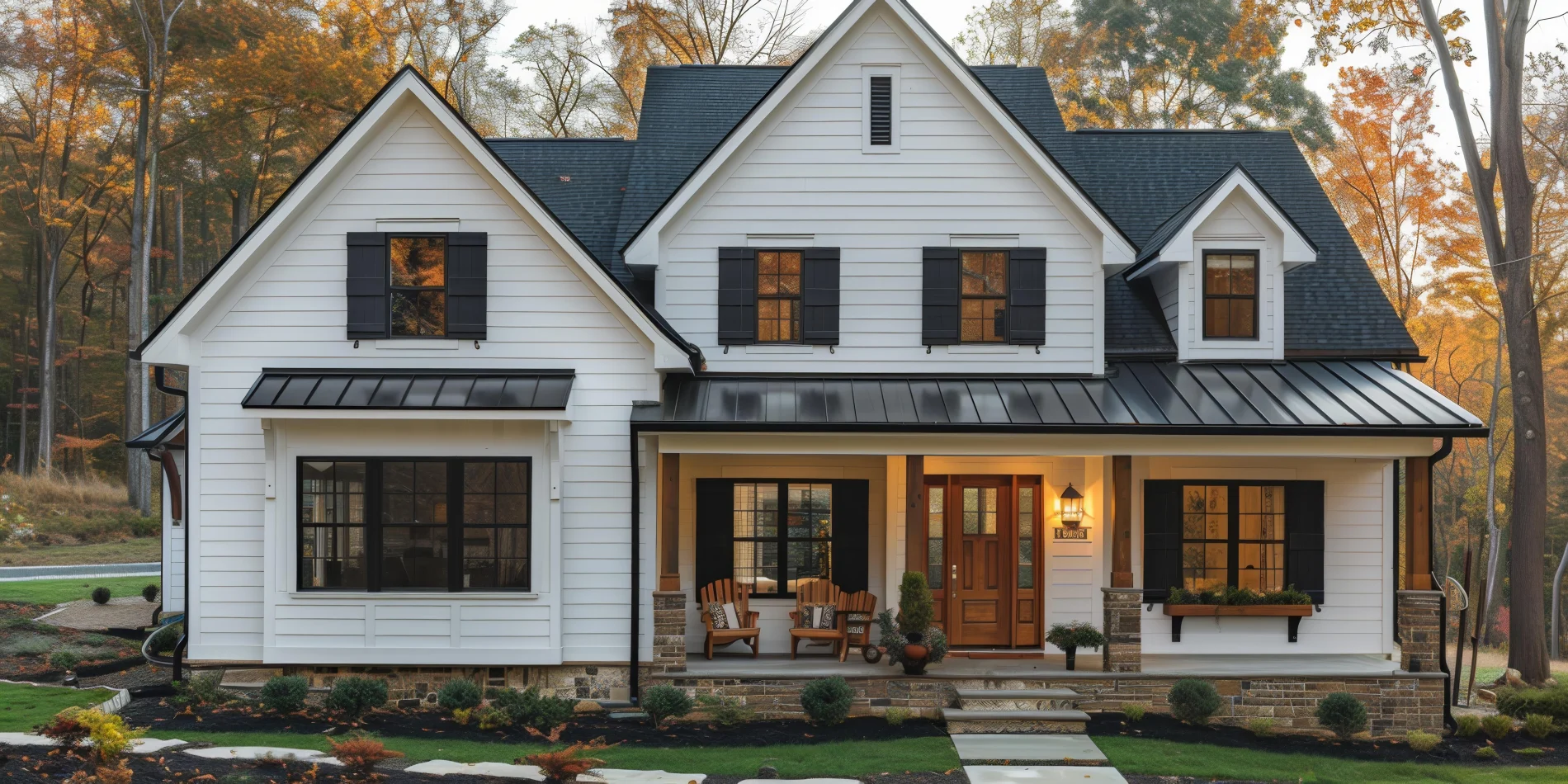 A two-story white house with stone and cement steps leading to the front porch, a wooden front door with glass inserts, black windows with black shutters, a stone base, wooden chairs on the porch, a metal roof over the porch, and a shingle roof.